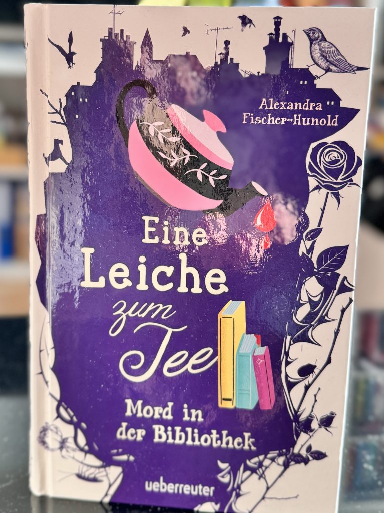 Eine Leiche zum Tee (2) - Mord in der Bibliothek 2 Auf dem Cover schüttet eine rosafarbene Teekanne Bluttropfen auf drei Bücher.