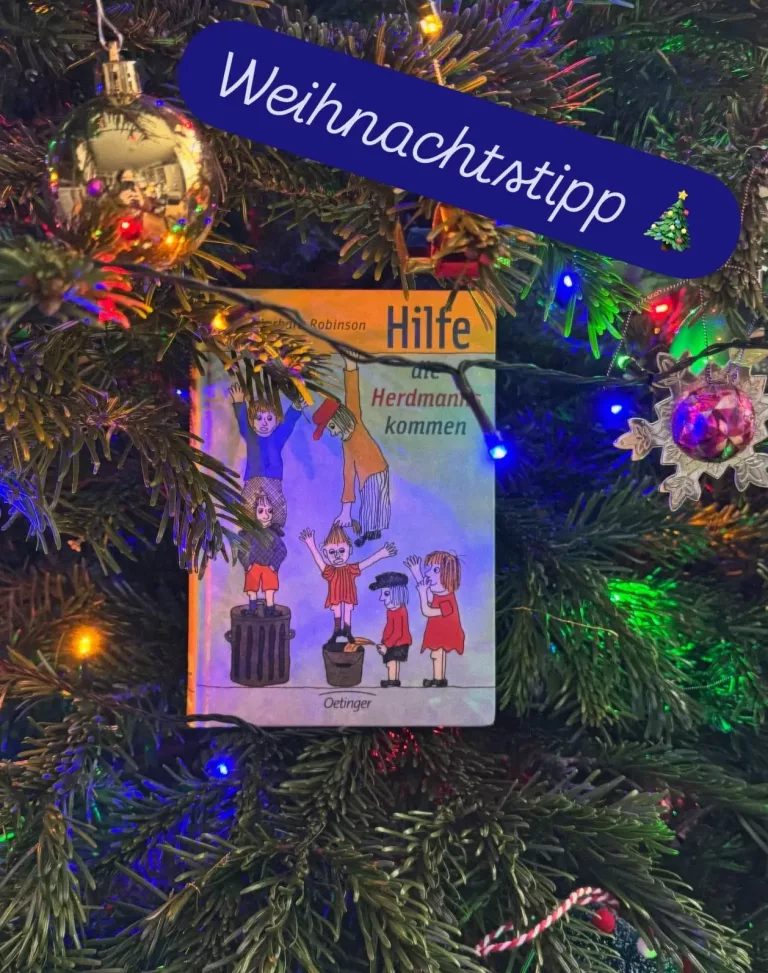 Das Buch mit den 6 Herdmann Kindern im Comicstil auf dem Cover hängt in einem geschmückten Weihnachtsbaum.