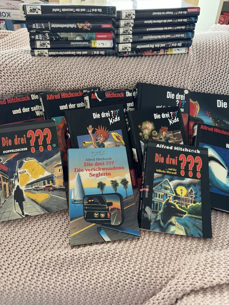 Viele verschiedene "Die drei ???" Bücher liegen verstreut auf einer Couch.