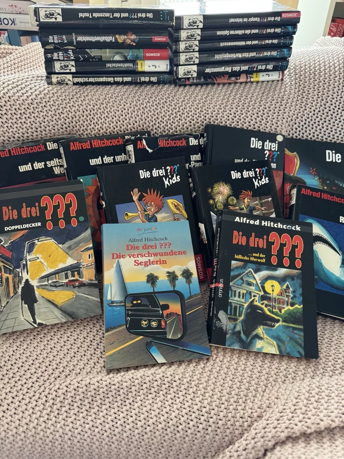 Viele verschiedene "Die drei ???" Bücher liegen verstreut auf einer Couch.