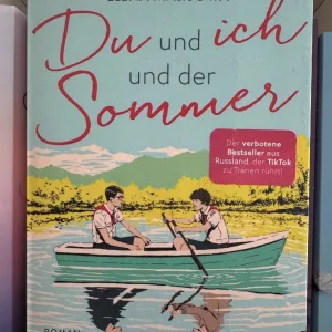 Die beiden Hauptcharaktere sitzen sich gegenüber in einem Ruderboot auf einem See. Von Elena Malisowa und Katerina Silwanowa