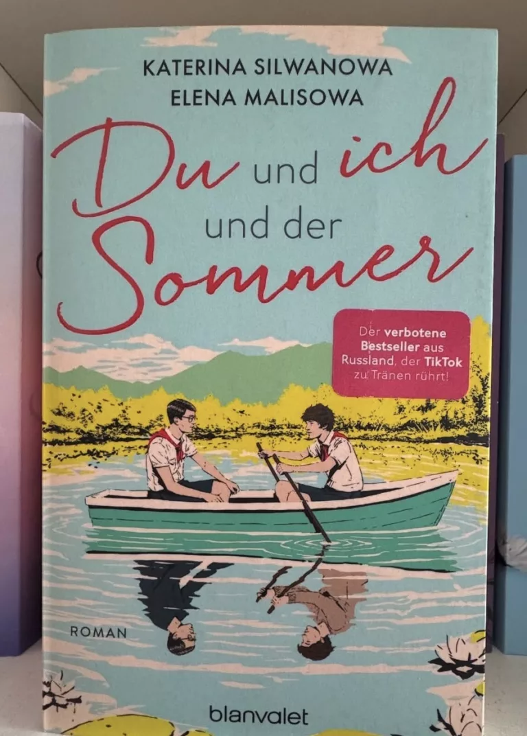 Die beiden Hauptcharaktere sitzen sich gegenüber in einem Ruderboot auf einem See. Von Elena Malisowa und Katerina Silwanowa