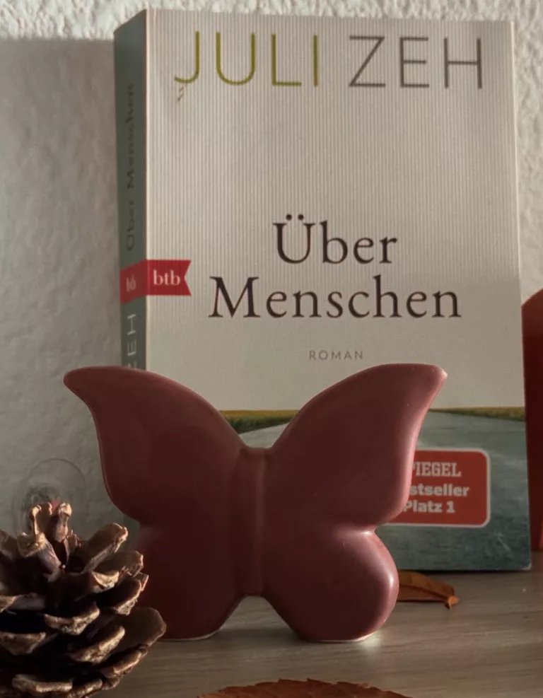 Das schlichte Cover des Buches "Über Menschen" von Juli Zeh zeigt eine von uns gerade weggehende Straße unter weißem Himmel auf der eine Katze liegt.