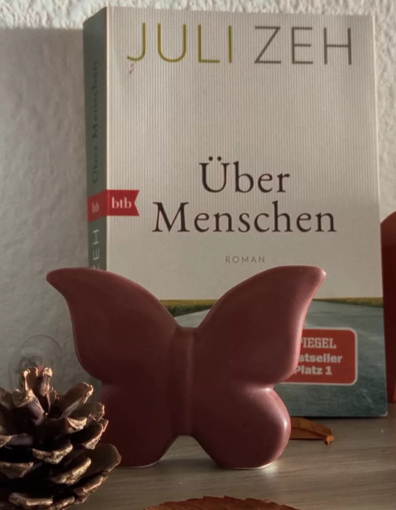 Das schlichte Cover des Buches "Über Menschen" von Juli Zeh zeigt eine von uns gerade weggehende Straße unter weißem Himmel auf der eine Katze liegt.
